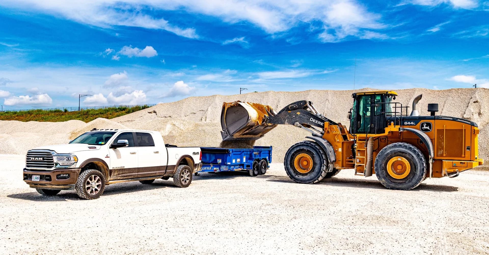 Ram truck hauling a Sure-Trac dump trailer loaded by a John Deere wheel loader